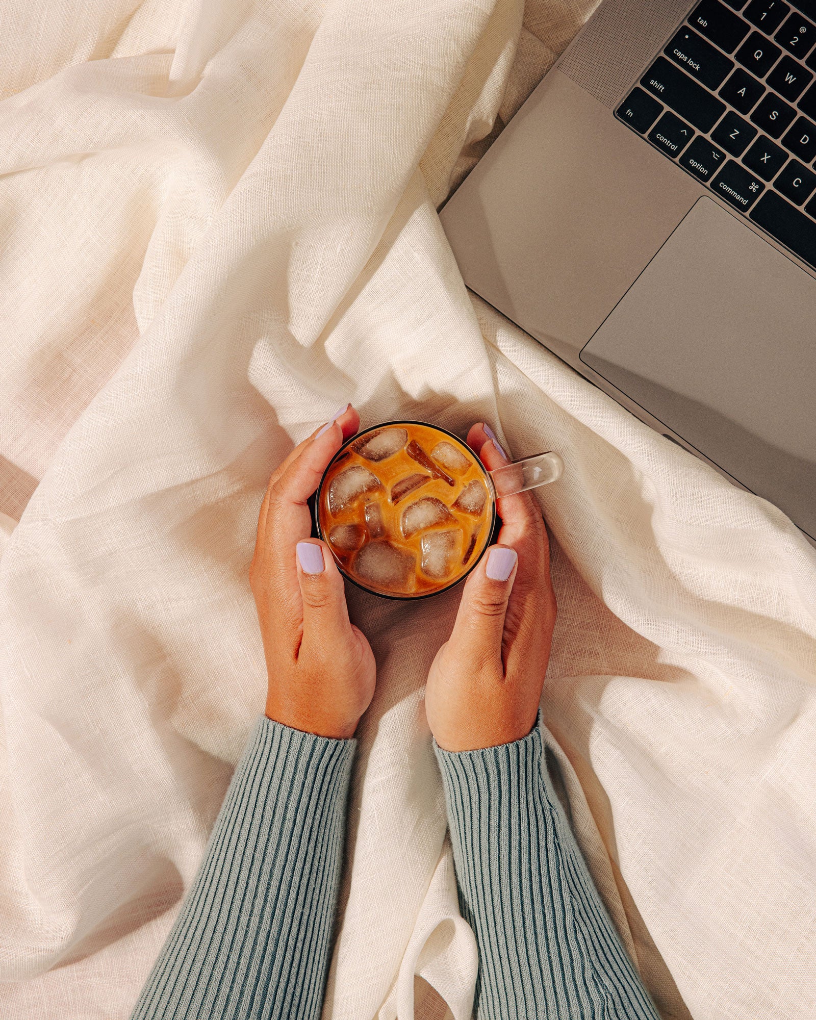 Hands cupping a mug of warm Flowstate coffee on a bed