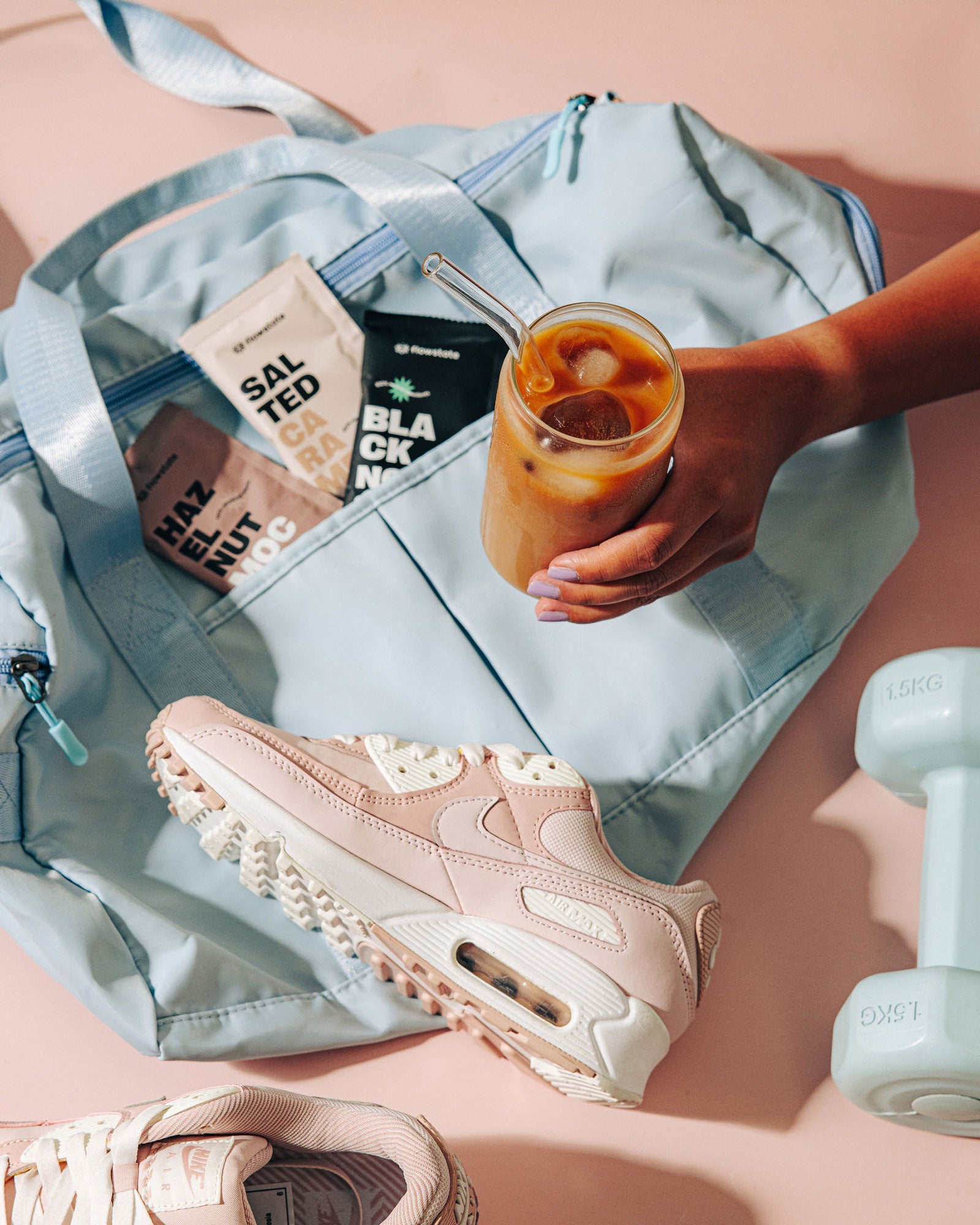 Glass of iced Flowstate coffee, gym bag, workout shoes and coffee sachets in the background